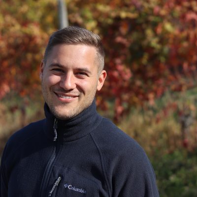 Thilo im Weinberg, im Herbst, lachend vor roten Rebzeilen